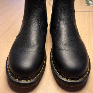 Svarta Chelsea boots från Dr. Martens - Säljer ett par svarta Chelsea boots 2976 från Dr. Martens med klassisk gul söm runt sulan. Har använt de några tillfällen för att se om de skulle gå ut sig lite men de är för små för mig. Inköpta på Johanssons i Göteborg, missade bytestiden därför får jag sälja dem. Kartong råkade slängas. Kvitto medföljer. 