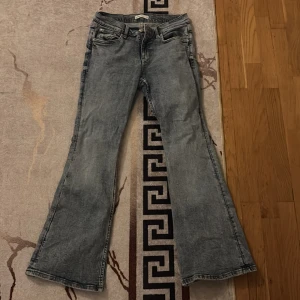 Bootcut jeans i ljusblå denim - Snygga bootcut jeans i ljusblå tvättad denim med klassisk femficksdesign och knappgylf. Byxorna har en utsvängd passform nedtill och är perfekta för dig som gillar retrovibbar och avslappnad stil.