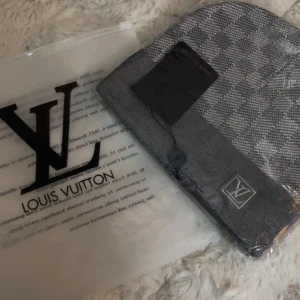 Grå rutig Louis Vuitton mössa - Snygg Mössa från Louis Vuitton i grått med klassiskt rutigt mönster och LV-logga framtill. mössan är tillverkad i mjukt stickat material och har en stilren, modern look. Perfekt för dig som vill ha en exklusiv accessoar med streetkänsla.