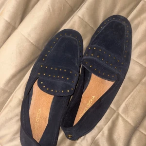 Mörkblå mockaloafers Agnes Cecilia - Snygga mörkblå loafers från Agnes Cecilia i mjuk mocka med platt sula. Skorna har dekorativa små guldfärgade nitar på ovansidan. Använda fåtal gånger och säljer pga att dem är för stora för mig. 
