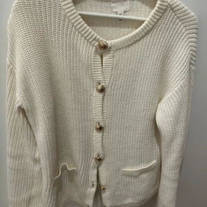 Krämvit stickad kofta med träknappar - Vit stickad kofta från H&M med snygga knappar framtill och två små fickor. Koftan har lång ärm, rund halsringning och en chunky ribbstickad struktur som ger en chill och trendig vibe. Storlek  S men passar äcen xs och m. Nyskick. Och superskön 