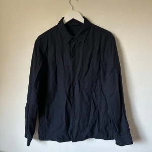 Mörkblå overshirt från Uniqlo, M - Mörkblå overshirt från Uniqlo i storlek M. Skjortan har klassisk krage, knappstängning framtill och en bröstficka. Materialet är en mix av bomull och linne som ger en skön känsla och lite struktur. Perfekt att bära som lager över t-shirt eller hoodie. 4F3