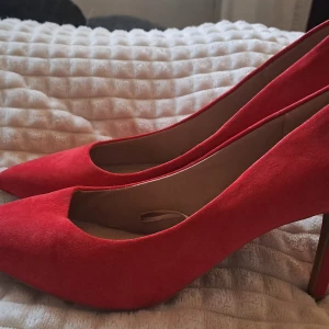 Röda mockapumps med spetsig tå - Snygga röda pumps i mocka med spetsig tå och smal klack. Skorna har en elegant siluett och är helt klädda i röd mocka, både på ovandel och klack. Perfekt för dig som vill sticka ut med färg och stil. Storlek 38
