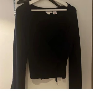 Svart omlottopp med långa ärmar - Säljer en svart omlottopp från NA-KD med långa ärmar och knyt i midjan. Toppen har en croppad passform och är perfekt för dig som gillar stilrena och enkla plagg. Materialet är mjukt och stretchigt, vilket gör den bekväm att bära.