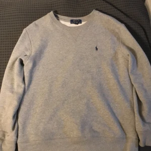 Grå tröja från Polo Ralph Lauren - Säljer en klassisk grå tröja från Polo Ralph Lauren. Den är i storlek S. Den har en minimal vit fläck på baksidan (finns på bild) men den är väldigt liten och kan mycket väl gå bort i tvätt.