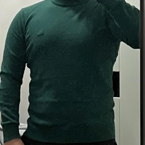 Grön polotröja - Säljer en snygg grön polotröja som är perfekt för kyligare dagar. Tröjan har en tight passform och är långärmad, vilket gör den både stilren och bekväm. Perfekt för både vardag och fest!