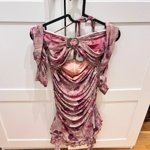 Rosa blommig klänning från 1JINN STUDIO - Säljer en superfin rosa klänning med blommigt mönster. Klänningen är mjuk, bra passform med volangdetaljer och valfri ärmdelar. Perfekt för fest eller en utekväll! Haft 2 gånger bara.Köpte kring 500kr. Passar bra för mig som bär s/36