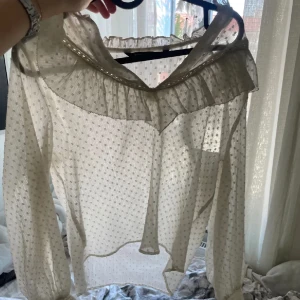 Vit blus från Zara - Säljer en superfin vit blus från Zara. Den har ett diskret prickigt mönster och volangdetaljer vid halsen. Blusen är långärmad och perfekt för både vardag och fest. Den är i ett lätt och luftigt material. Obv bild från gammal ägaren!💕skriv innan köp