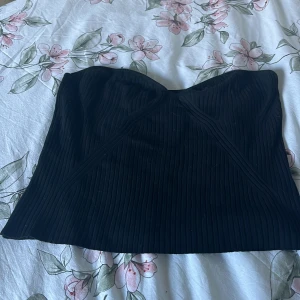Svart ribbad tubtopp från Lindex - Säljer en snygg svart ribbad tubtopp från Lindex. Perfekt för en kväll ute eller som en stilren bas i garderoben. Toppen är i storlek L!