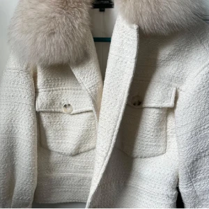 Vit meotine jacka!! - Säljer min vita meotine jacka som ger en Elegant och snygg vibe. vit kappa med en lyxig pälsdetalj vid kragen. Jackan har en strukturerad yta och stora knappar framtill. Perfekt för att ge en stilren touch till din outfit.