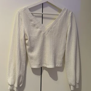 Vit ribbad tröja med v-ringning - Säljer en stilren vit tröja med v-ringning och ribbad struktur. Tröjan har långa ärmar och en croppad passform, perfekt för både vardag och fest. Ett måste i garderoben för den som gillar enkel elegans.