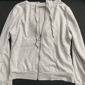 Grå hoodie med dragkedja - Säljer en bekväm grå hoodie med dragkedja framtill. Tröjan har långa ärmar och en klassisk huva. Perfekt för en avslappnad stil.