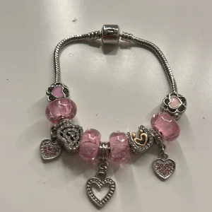 Silverarmband med rosa berlocker - Charmigt silverarmband med flera rosa berlocker och hjärtformade detaljer. Armbandet har en mix av glittriga och släta berlocker, vilket ger en fin kontrast. Perfekt för att lägga till en romantisk touch till din stil.