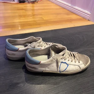 Vita sneakers från Philippe Model - Snygga vita sneakers från Philippe Model med grå detaljer och blå accenter. Skorna har en klassisk snörning och en bekväm sula. Perfekta för en avslappnad stil.