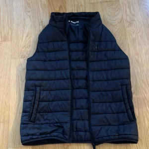 Svart väst från Everest - Säljer en svart väst från Everest. Västen har en dragkedja framtill och två fickor på sidorna. Perfekt för kyligare dagar och enkel att matcha med andra plagg.