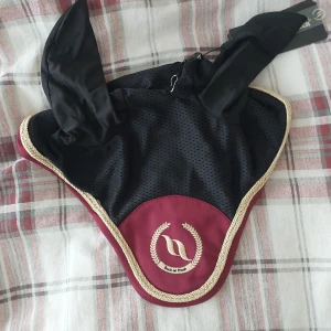 Svart och vinröd huva från Back on Track - Snygg huva från Back on Track i svart och vinrött med broderad logga. Tillverkad i polyester och elastan med guldfärgad kant. Perfekt för ridning. Original pris 469kr💞