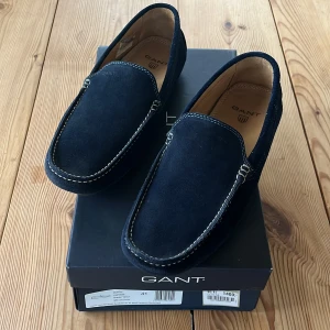 Mörkblå mockaloafers från Gant - Snygga mörkblå loafers från Gant i mjuk mocka. Skorna har en stilren design med kontrasterande vita sömmar och en bekväm sula. Perfekta för en avslappnad men elegant look.