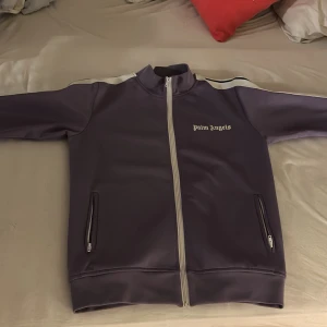 Palm Angels kofta  - Snygg lila track jacket från Palm Angels med vit dragkedja och logga på bröstet. Jackan har långa ärmar och ribbade muddar. Perfekt för en sportig look. Helt ny, pris kan diskuteras!