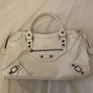 Vit handväska med dragkedja - Snygg vit handväska i skinn med coola detaljer och dragkedja. Perfekt för att ge din outfit en stilren touch. Väskan har en praktisk storlek och är lätt att bära med sig. Lite smutsig därav priset
