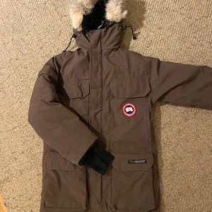 Canada Goose Expedition - Brun Canada Goose Expedition Parka i unisex modell stl xxxs vilket motsvarar stl 34-38 skulle jag säga.  Jackan är välanvänd och har lite slitningar (se bild). Pälsen är också lite sliten. Men är mycket varm och intakt i övrigt. De äldre modellerna av Canada Goose sägs ha mer och högre kvalitet på dunfyllning än de nyare. Klarar -30grader.