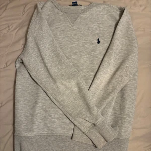 Grå tröja från Polo Ralph Lauren stl M (10-12år) - Säljer en stilren grå tröja från Polo Ralph Lauren med det klassiska broderade logotypen på bröstet. Tröjan har långa ärmar och en rund  halsringning, perfekt för en avslappnad look. Stl M 10-12 år. Fint skick knappt använd. 