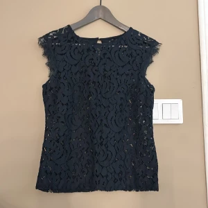 Marinblå spetsblus - Elegant svart spetsblus med vackert mönster och ärmlös design. Perfekt för en stilren look med en knappdetalj i nacken.