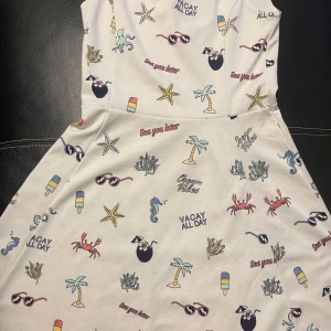 Vit klänning med somrigt mönster från Hm - Säljer en vit klänning från hm med ett lekfullt somrigt mönster av palmer, sjöhästar, krabbor och solglasögon. Klänningen är ärmlös och har en avslappnad passform, perfekt för varma dagar. Den har en rund halsringning och är gjord i ett mjukt material.