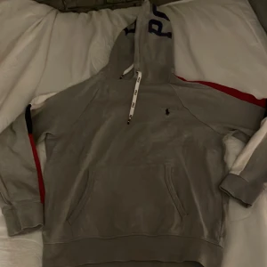 Grå hoodie från Polo Ralph Lauren - Säljer en stilren hoodie från Polo Ralph Lauren med logga på bröstet och stor text på huvan. Perfekt för en avslappnad look. Perfekt för både finare tillfällen och när man vill ta det lugnt. Storleken är M men passar S också! Priset kan diskuteras