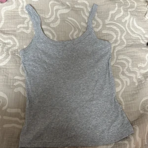 Grå ribbad linnetopp från Gina Tricot - Säljer en stilren grå ribbad linnetopp från Gina Tricot. Perfekt för en avslappnad look. Toppen har breda axelband och en klassisk rund halsringning.