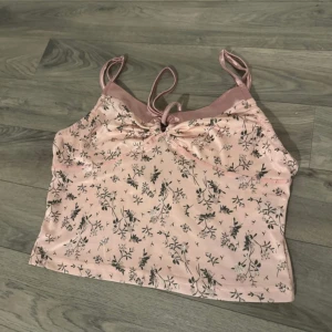 Rosa blommig linne - Säljer ett sött rosa linne med blommigt mönster och smala axelband. Linnet har en knytning framtill och är perfekt för varma sommardagar.