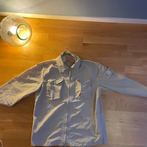 STONE ISLAND OVERSHIRT - Nu säljer vi den här feta Stone Island jackan/overshirten. Den är tunn men är i någon form av jacka material. Skickas inom 48h, hör av er för fler frågor eller bud! OBS! Jackan är i storlek L men den sitter lite litet på mig som är 1.90 och väger 60kg!