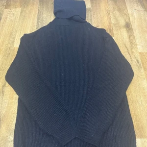 Svart stickad polotröja - Säljer en stilren svart stickad polotröja med ribbad design. Perfekt för kyliga dagar med sin höga krage och långa ärmar. Ett måste i garderoben för en klassisk look. Priset går att diskuteras 