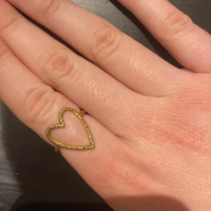 Guldfärgad hjärtring - Snygg guldfärgad ring med ett öppet hjärta som design. Ringen är justerbar (bild 2) och passar därför alla. Köpt från Caroline Svedbom. Köpte för 599kr. 