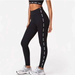 Svarta leggings från Stronger med logotyp - Snygga svarta leggings från Stronger med hög midja och logotyp längs sidorna. Perfekta för träning eller en avslappnad dag. 
