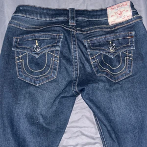 Mörkblå jeans från True Religion - Säljer dessa snygga mörkblå jeans från True Religion i strl 27 då de var alldeles för stora, byxorna har inga skador och ser helt nya ut  Byxorna har bootcut-stil, Märkets ikoniska logga syns på bakfickorna. 💞
