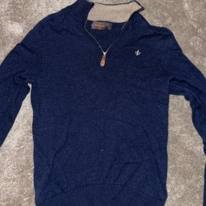 Mörkblå tröja med dragkedja från Morris  - Snygg mörkblå tröja från Morris med en liten broderad logga på bröstet. Tröjan har en dragkedja vid halsen och är tillverkad i ett mjukt material. Perfekt för kyligare dagar.