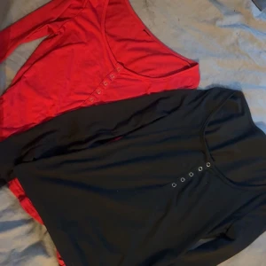 Svart och röd långärmad topp med knappar - Två stilrena långärmade toppar i svart och rött med knappdetaljer framtill. Perfekta för en casual look eller att klä upp med accessoarer. Två för 80kr