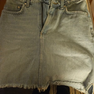 Jeanskjol från H&M - Säljer en snygg jeanskjol från H&M i ljusblå denim. Kjolen har en rå kant nertill och klassisk femficksdesign. Perfekt för en avslappnad stil.