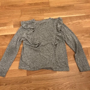 Grå tröja med volangdetaljer från Lindex - Säljer en stilren grå tröja från Lindex med volangdetaljer längs ärmarna. Är inte lika sjuk som man föreställer sig men fortfarande bra att bära💞