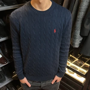 Mörkblå stickad tröja från Polo Ralph Lauren - Säljer en snygg mörkblå stickad tröja från Polo Ralph Lauren med det klassiska röda logotypen på bröstet. Tröjan har ett kabelstickat mönster. |nästintill helt ny| sitter fint längst kroppen. St:M. Först till kvarn🤙