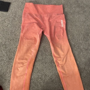 Rosa leggings från Gymshark - Snygga rosa leggings från Gymshark med ombre-effekt. Perfekta för träning med högmidjad passform som ger bra stöd. Materialet är stretchigt och bekvämt, vilket gör dem idealiska för alla typer av aktiviteter.