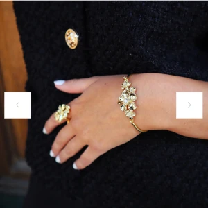 Guldarmband från Ioaku - Elegant guldarmband från Ioaku med blommiga detaljer. Armbandet har en tunn design med en vacker blomma i mitten, perfekt för att ge en touch av glamour till din outfit. Helt slutsåldt och svårt att få tag på. 