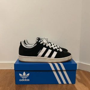 Svarta Adidas Campus 80s - Snygga svarta Adidas Campus 80s sneakers med vita detaljer och klassiska tre ränder på sidan. Skorna har en vit sula och snörning. Perfekta för en stilren look. Säljer pga för liten storlek.