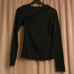 Svart långärmad topp med asymmetrisk design - Snygg svart topp med lång ärm och unik asymmetrisk halsringning. Perfekt för en stilren look med en twist. Materialet är ribbat vilket ger en skön passform.