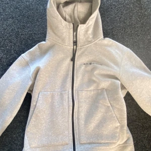 Grå hoodie från Sail Racing - Säljer en snygg och bekväm grå hoodie från Sail Racing. Den har en dragkedja framtill och två stora fickor. Perfekt för kyliga dagar och passar bra till både vardag och fritid.