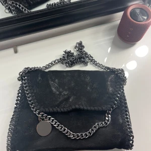 Svart axelväska med kedjedetaljer - Säljer en snygg svart axelväska med coola kedjedetaljer. Väskan har en glittrig yta och ett stort fack med leopardmönstrat foder. Perfekt för både vardag och fest! 🖤