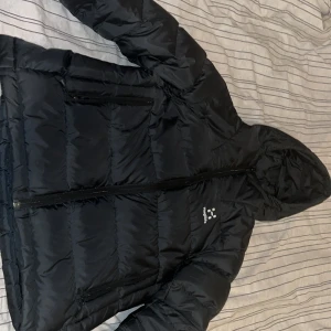 Svart dunjacka från Haglöfs - Säljer en svart dunjacka från Haglöfs i storlek M för dam. Jackan är perfekt för kalla dagar med sin pufferstil och har en praktisk huva. Den är långärmad och har en dragkedja framtill. Superbra skick och redo för vintern!