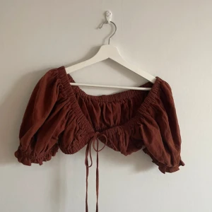 Brun croppad blus med puffärmar - Säljer en superfin brun croppad blus med puffiga kortärmar och knytning framtill. Blusen har en elastisk kant som ger en bekväm passform.