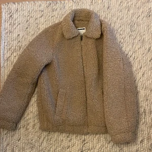 Beige teddyjacka från Noisy May - Säljer en supermysig beige teddyjacka från Noisy May i storlek S. Jackan har en dragkedja framtill och är perfekt för kyliga höst- och vinterdagar. Den är långärmad och gjord i ett fluffigt teddy-material som håller dig varm och stilren. 