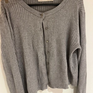 Ribbstickad kofta  - Grå ribbstickad kofta! Den är i bra skick förutom en liten spricka (se andra bilden) de är inget man tänker på när man har den på eller som syns men den finns där! 